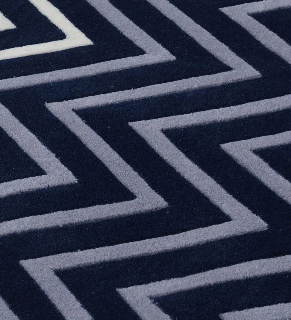 A close-up of a textured rug featuring a bold geometric chevron pattern in dark navy blue and light gray.