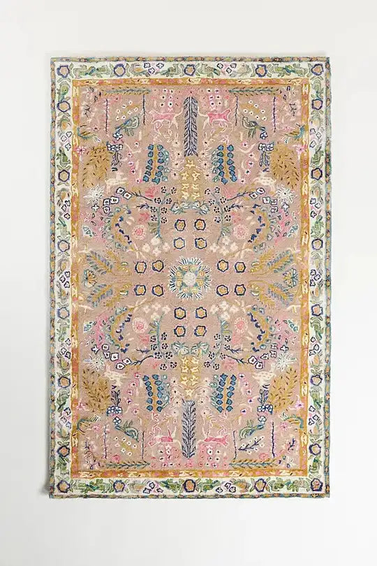 A rectangular vintage-style area rug with an intricate floral and medallion pattern in soft pastel tones, including pink, beige, green, blue, and yellow, shown hanging against a plain white wall.