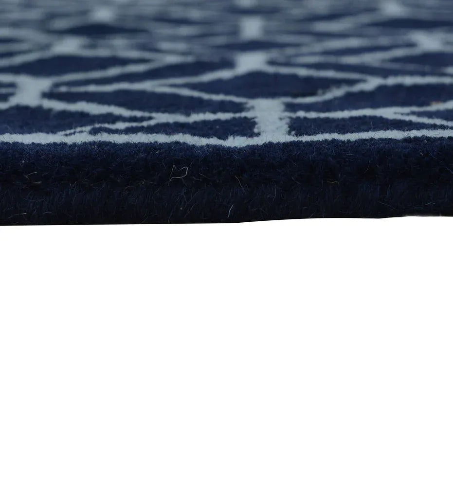 Close-up of a dark navy blue rug with a light beige or off-white geometric pattern, showing the texture and edge of the pile against a white background.