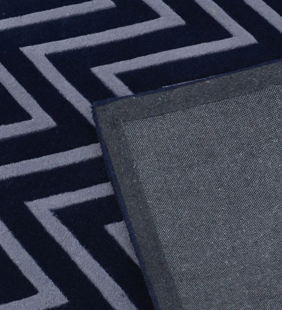 Close-up of a dark navy rug with a light gray geometric chevron pattern, showing the pile texture and a dark gray woven border.