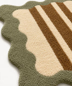 Close-up of a textured rug with green, beige, and brown stripes on a white background